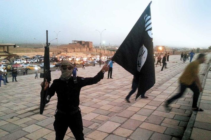 A fighter holds an Islamic State flag and a gun on a street in Mosul