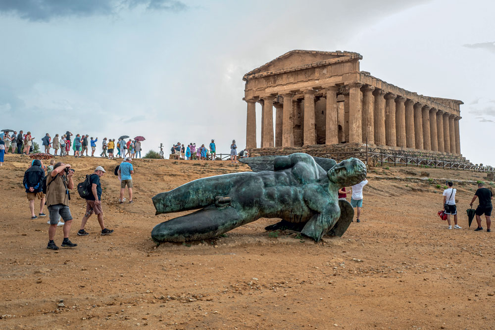 Igor Mitoraj's statue Fallen Icarus and the Greek Temple of Concordia at the Valle dei Templi, Agrigento, Italy 