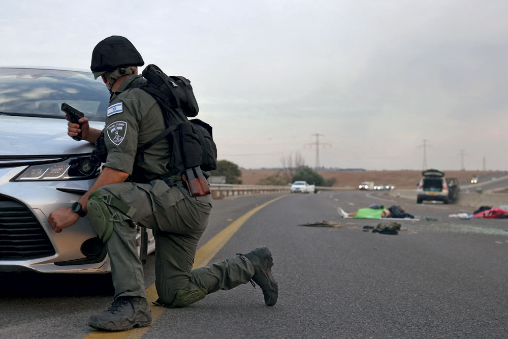 An Israeli soldier takes cover behind a car near the Gevim kibbutz, close to the Gaza border, October 7, 2023 